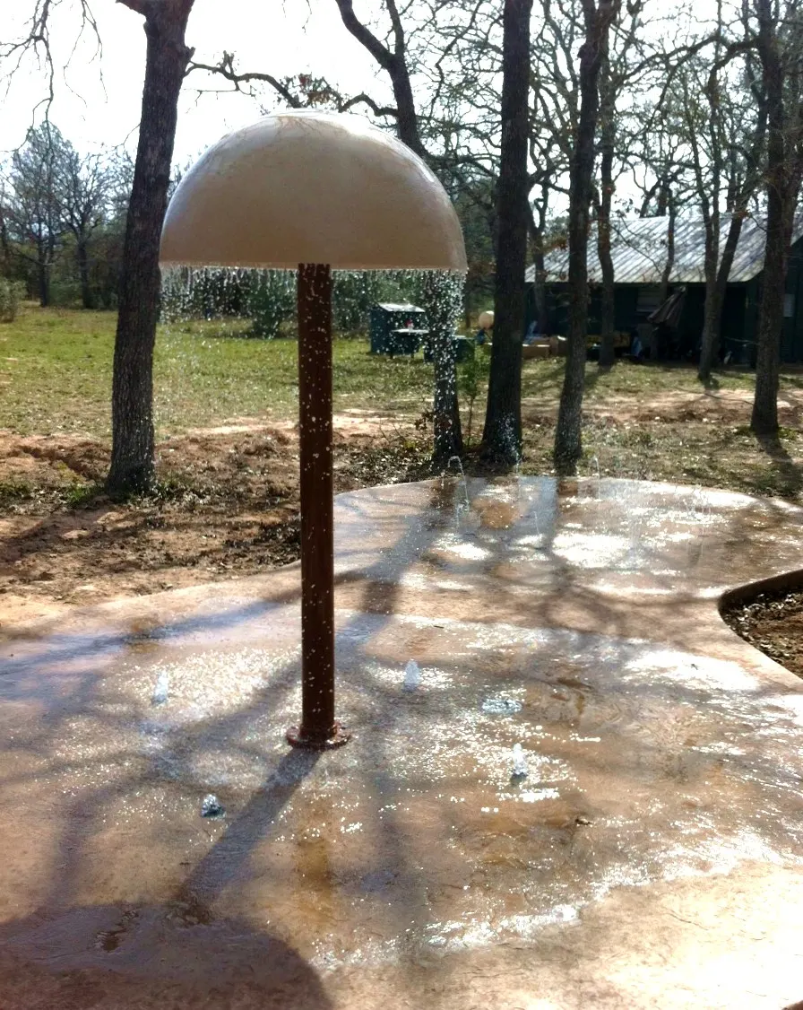 Water mushroom raining onto a small backyard splash pad under trees