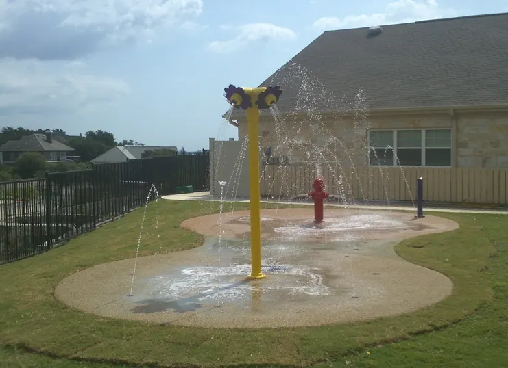 Small splash pad with a yellow water umbrella and ground jets surrounded by lawn